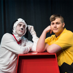Person in dog costume and person in Charlie Brown costume leaning on red dog house